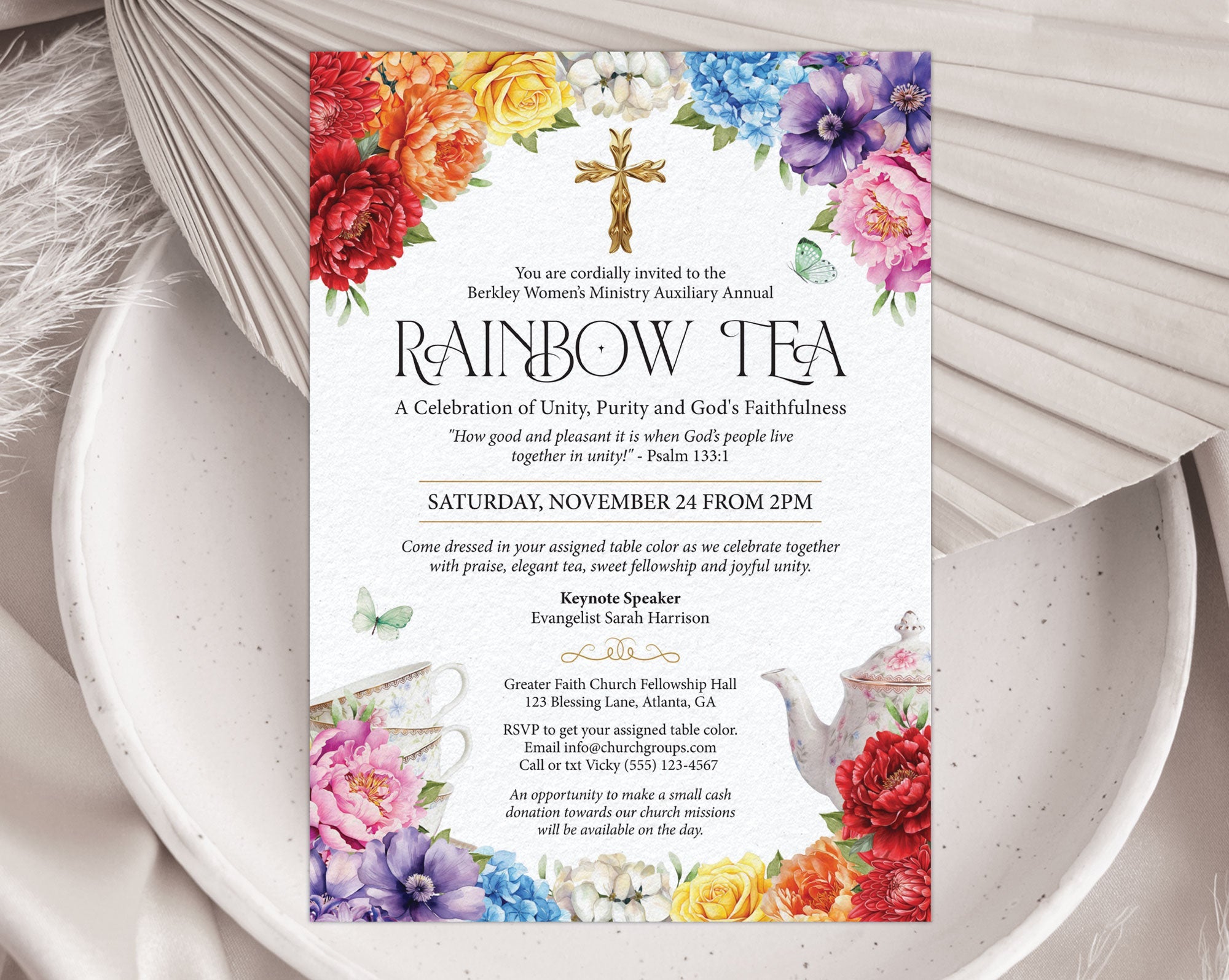 A pretty Church Rainbow Tea invitation with gold cross, teapot and tea cups, laying on a plate and dried leaf