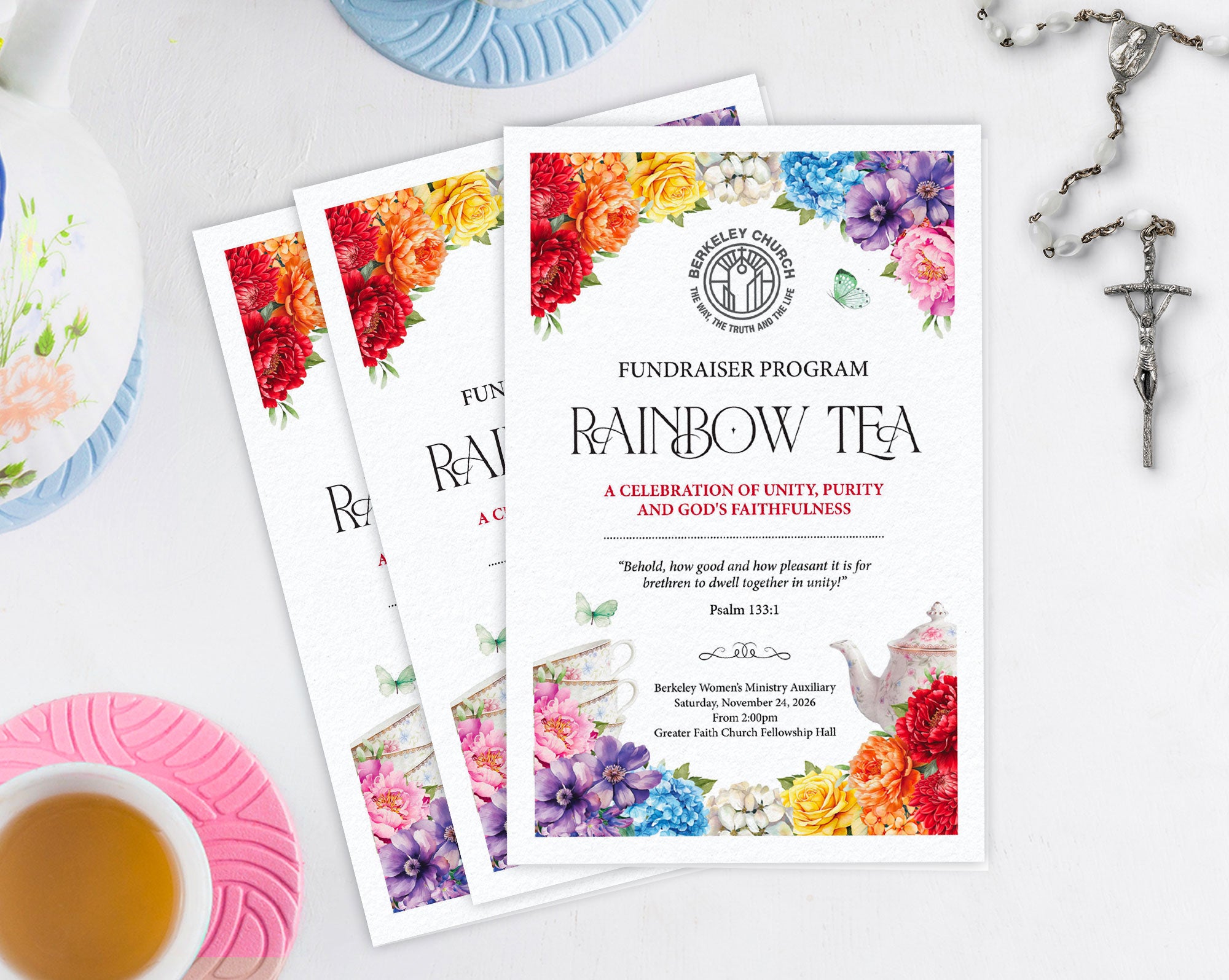 Three printed letter sized folded program flyers for a church fundraiser event titled 'Rainbow Tea' are arranged on a white surface with decorative props including a teacup, saucer, flowers, and a cross.