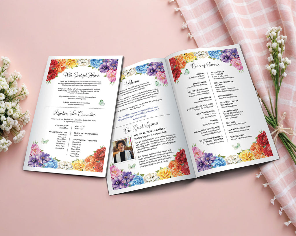 An open 11 x 8.5 folded Rainbow tea church program booklet displayed on a soft pink surface, surrounded by white flowers and a pink plaid cloth. The booklet has colorful floral watercolor borders and printed ceremony text.