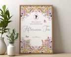 Small Bridgerton inspired afternoon tea digital welcome sign in a wooden frame leaning up against a beige wall next to some greenery in vases