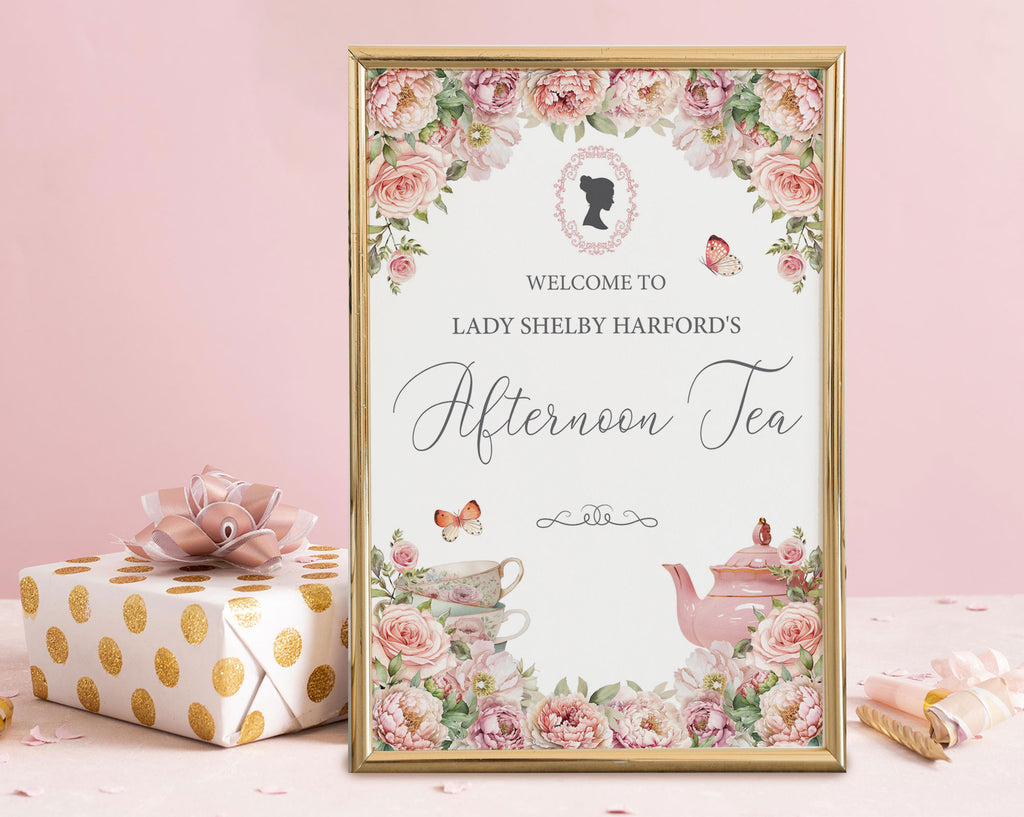 elegant sign for an afternoon tea event with floral design, regency cameo and teapot illustration in a gold frame leaning on a pink background next to a wrapped gift