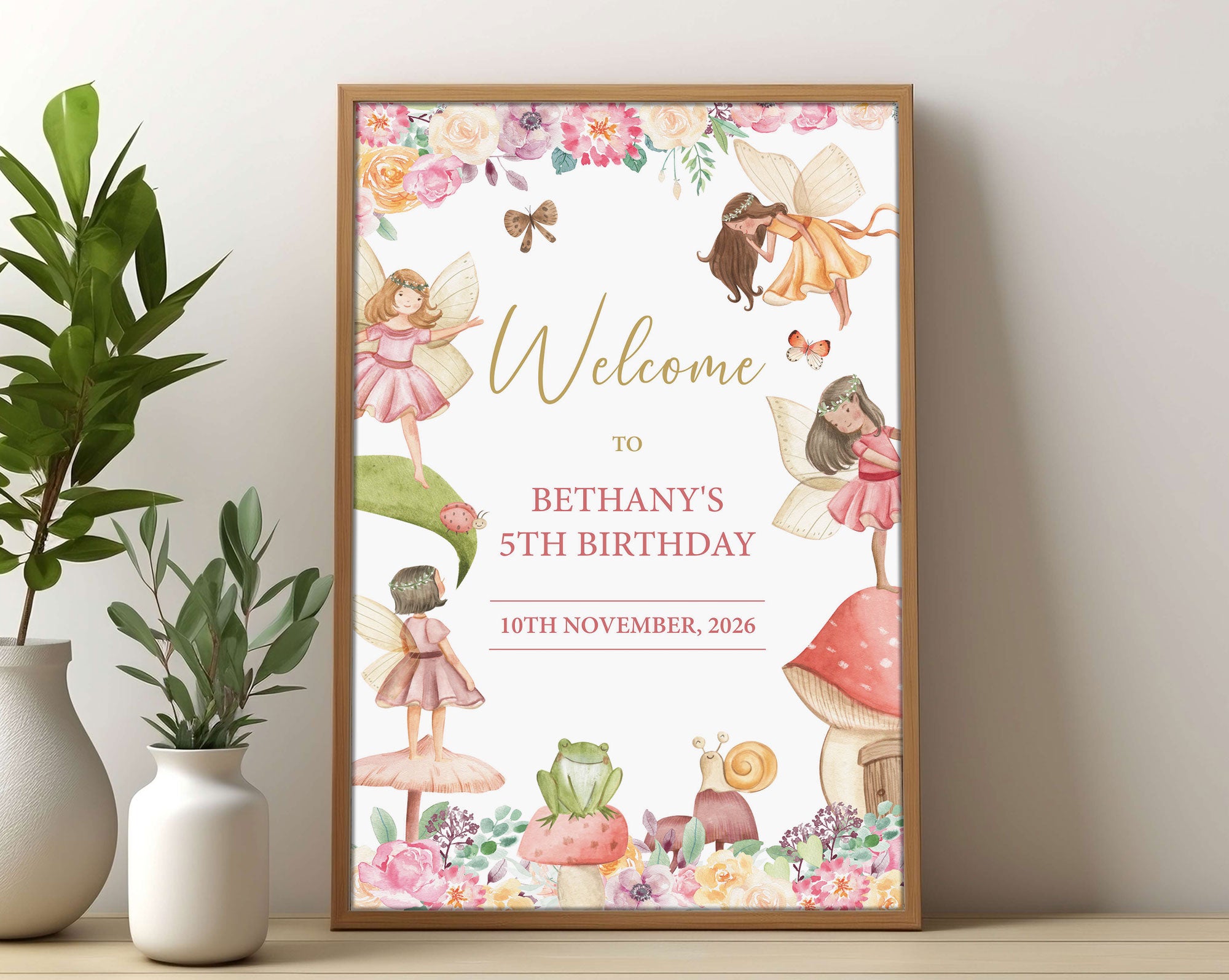 an A3 fairy birthday party welcome sign in a wooden frame leaning up against a beige wall next to greenery in two vases
