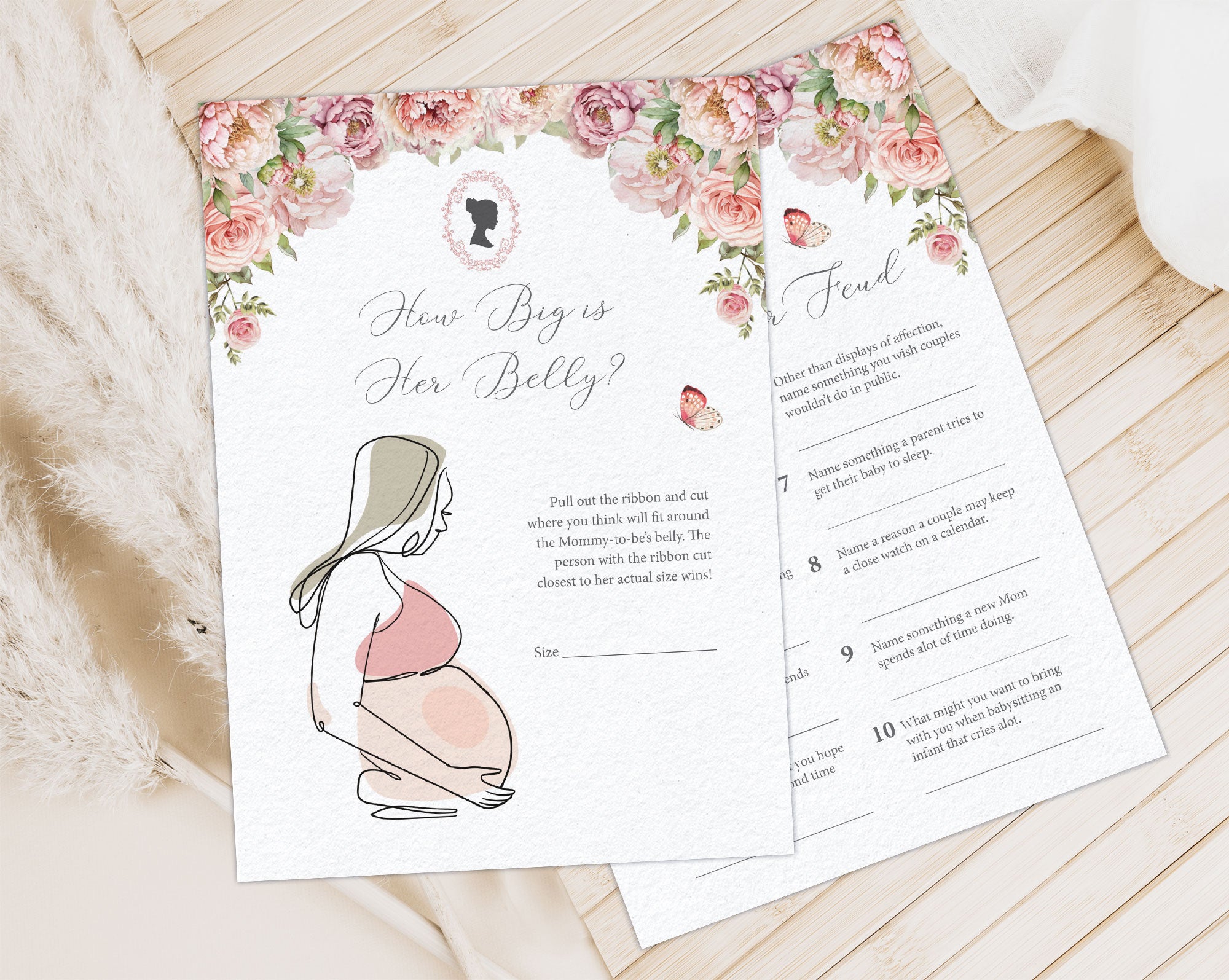 2 blush pink flower baby shower game cards laying on a wooden background next to a cloth and some dried plants