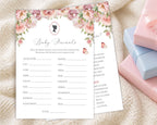 two blush pink baby shower game cards, one titled 'baby shower feud' laying on a cream blanket next to some pink and blue wrapped gifts