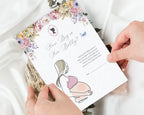 two hands holding a 'how big is her belly' baby shower game card with a white silk cloth in the background