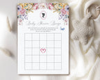 a pastel regency style 'baby shower bingo' card laying on a cream cloth with a baby teether next to it
