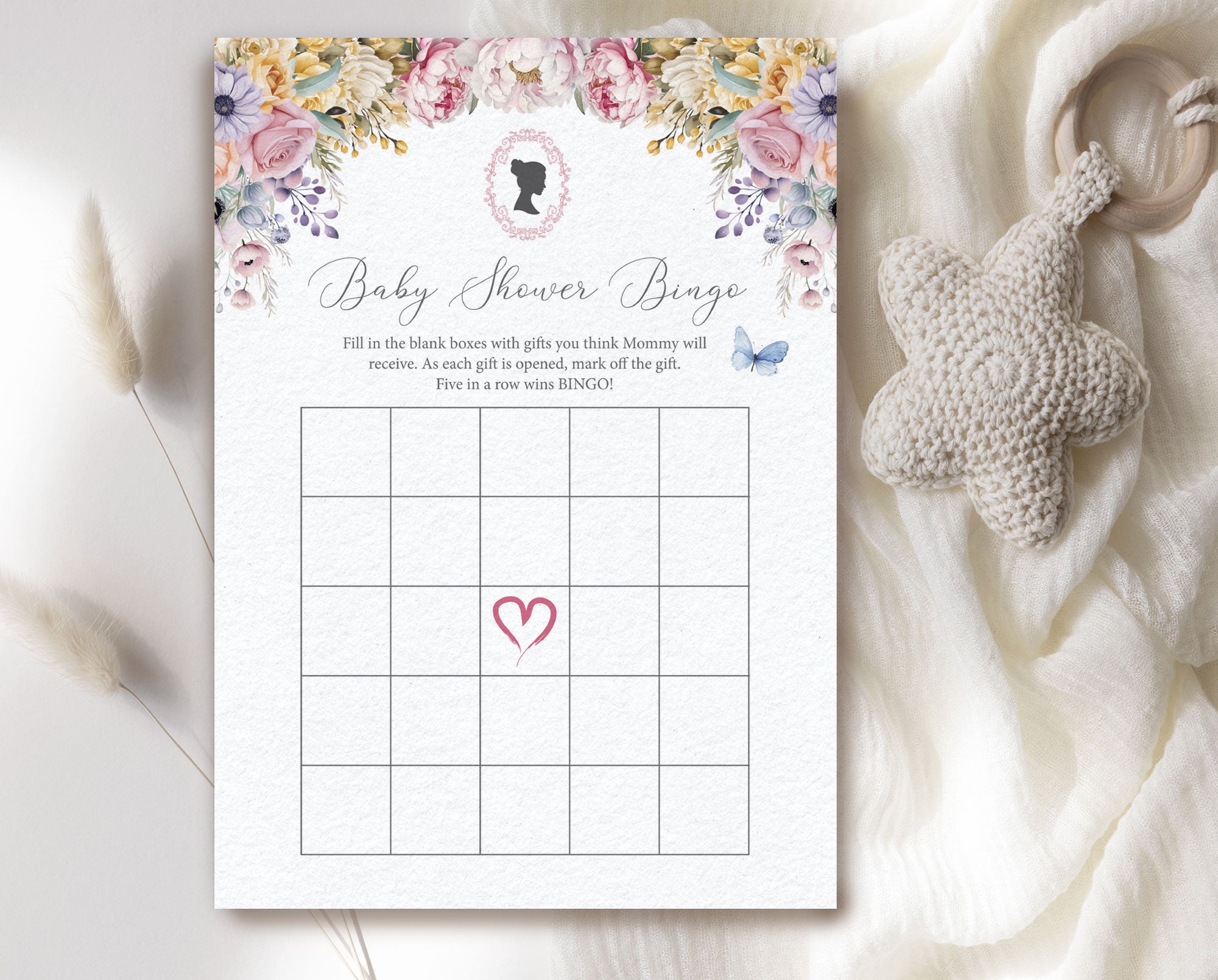 a pastel regency style 'baby shower bingo' card laying on a cream cloth with a baby teether next to it