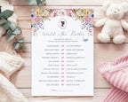 A baby shower game card titled 'would she rather' laying on a wooden background, next to a white teddy bear, a pink and a white blanket and some eucalyptus leaves