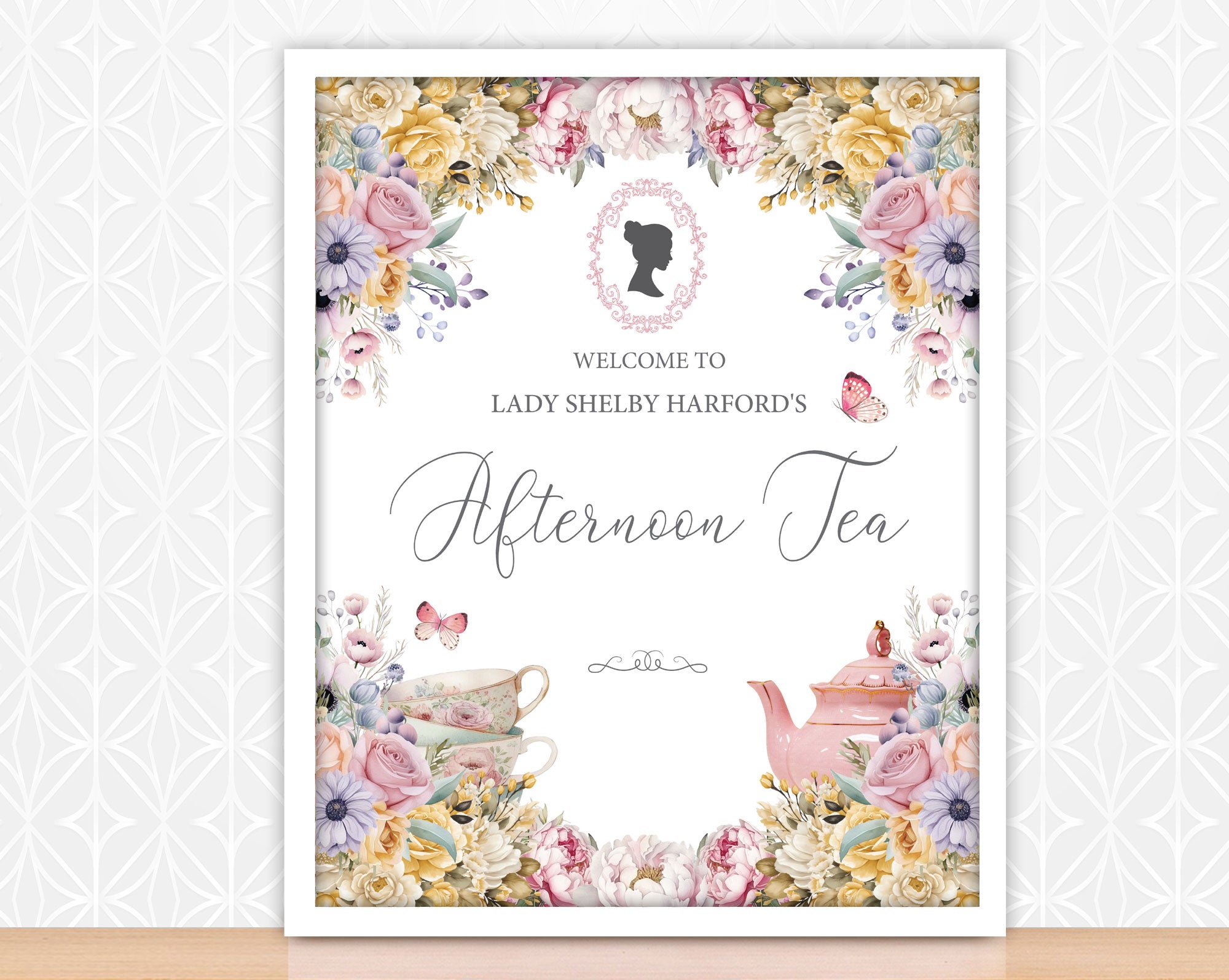 pink blue and yellow flower sign for an afternoon tea event with floral design and cameo, in a frame leaning up against some patterned white wallpaper