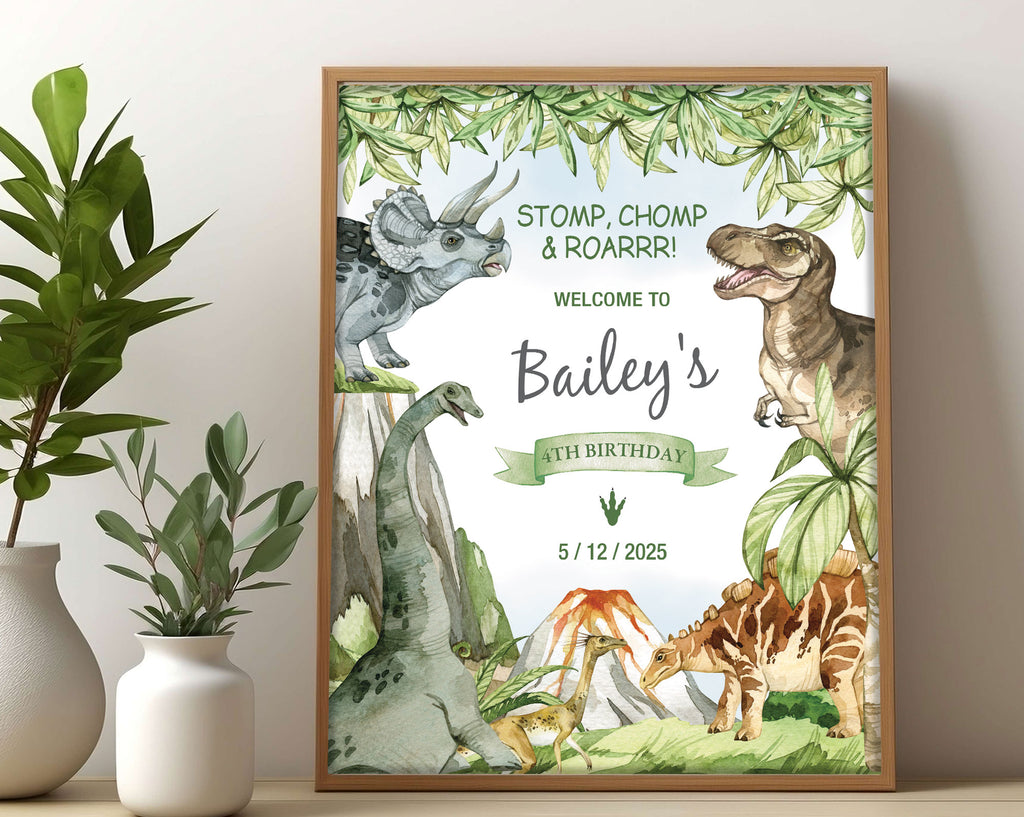 a kid's dinosaur party welcome sign with various dinosaurs, volcano and prehistoric forest graphics, in a wooden frame, leaning on a beige wall next to two white vases with greenery