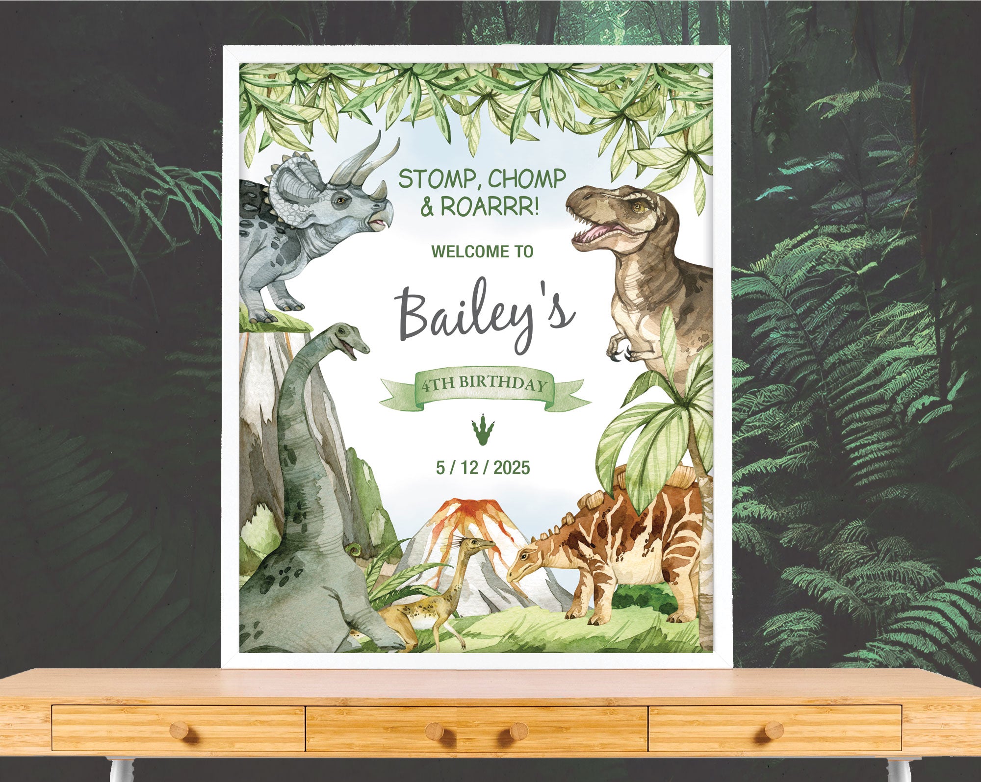 a dinosaur party welcome sign with volcano in a white frame leaning on a forest wallpaper wall on a wooden table