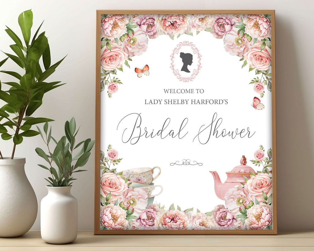 pretty Bridal shower sign with blush pink flowers and regency cameo in a wooden frame, leaning up against a beige wall next to some greenery in vases