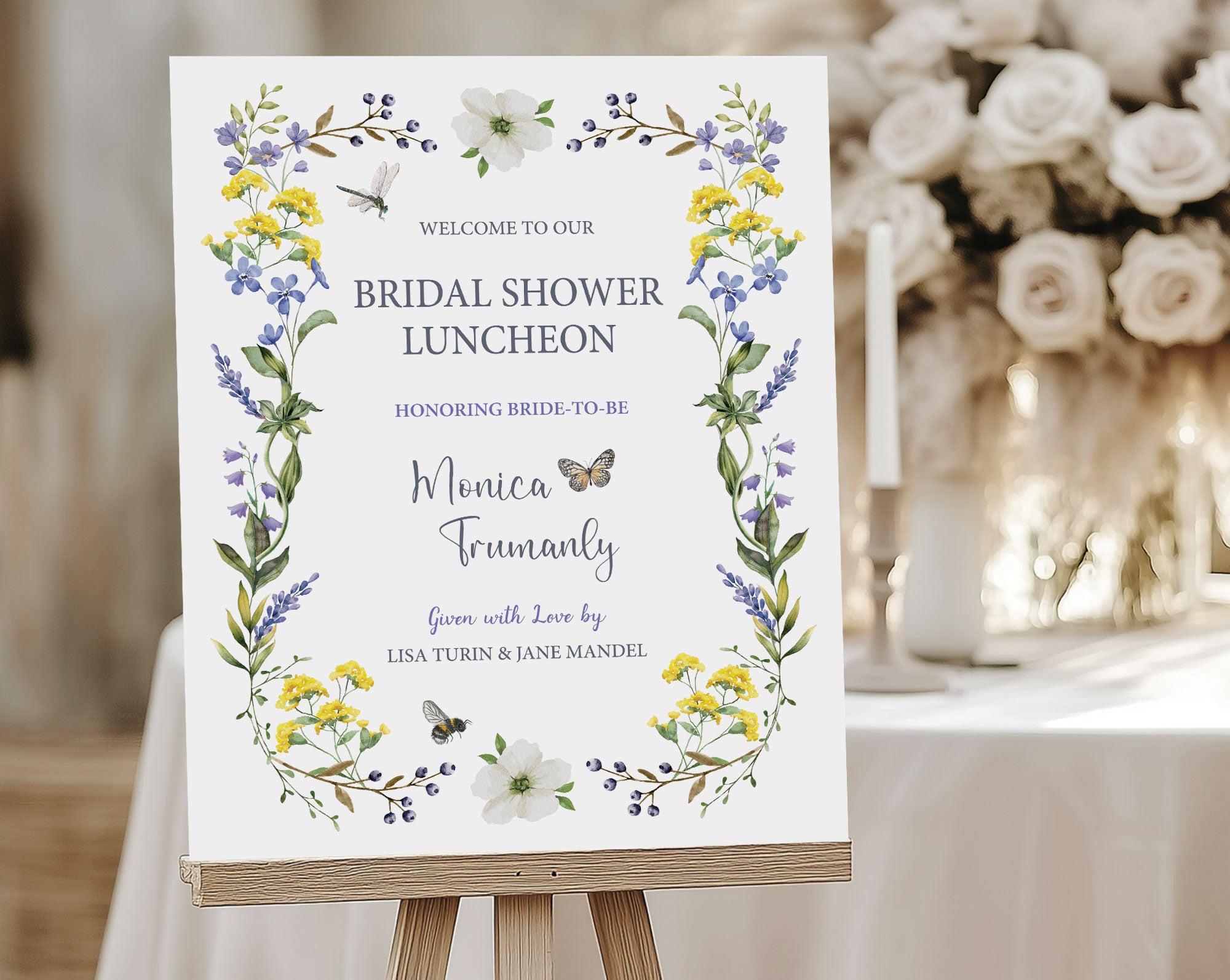 a wildflower welcome sign with butterfly, dragonfly and bee, on a wooden easel, in front of a table with candles and white flowers