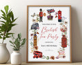 british tea party welcome sign with london icons in red and black in a wooden frame leaning on a wall on a table next to a vase with greenery