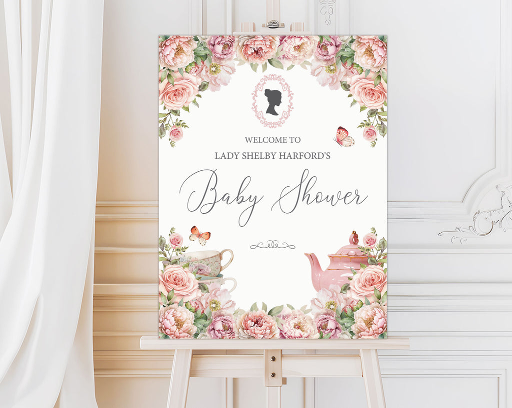 elegant blush pink entrance sign for a baby shower with teapot and cameo on a wooden easel in front of a white panelled wall and curtain