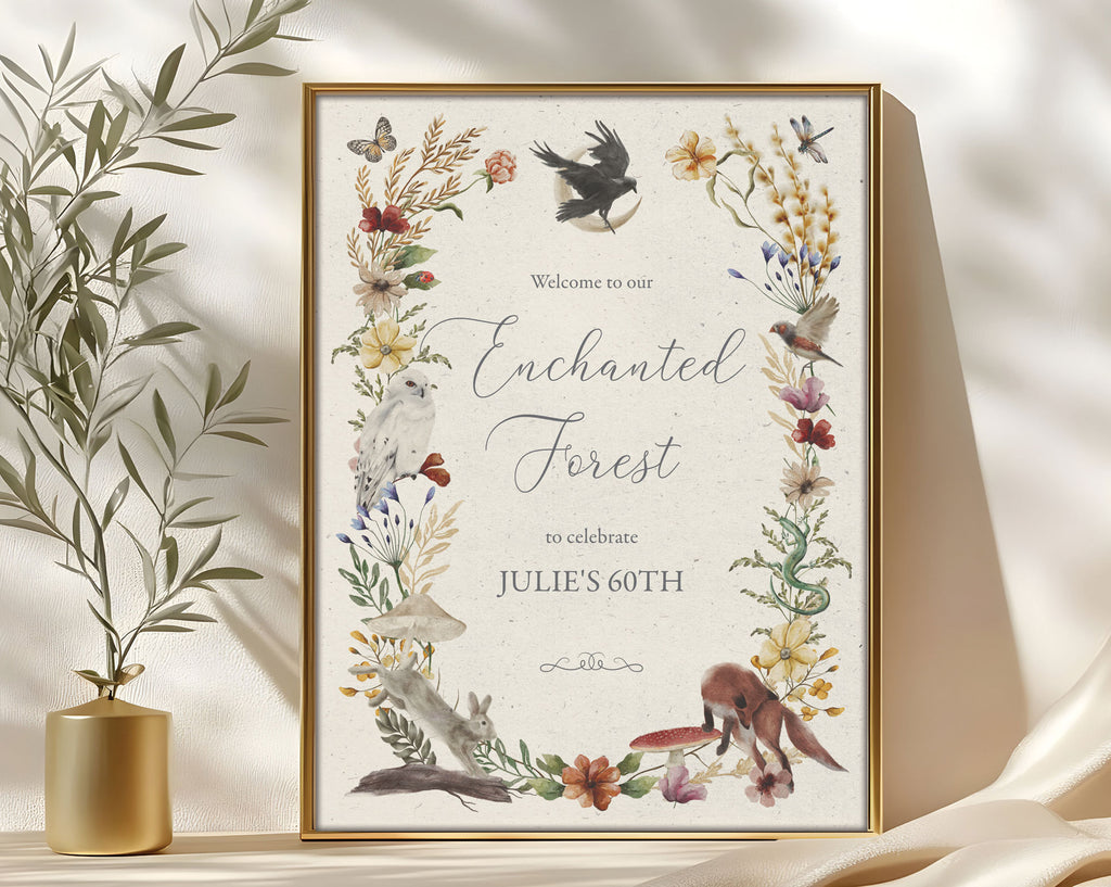 enchanted 18 x 24 sign in a gold frame with raven, forest animals and flora and fauna, leaning up against a beige wall next to some greenery in a gold vase