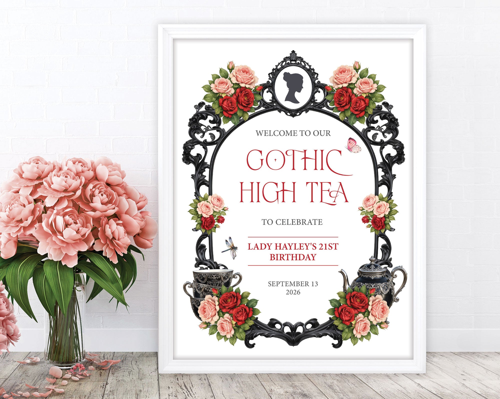 a red black and pink gothic high tea sign in a white frame leaning up against wall next to some blush pink flowers