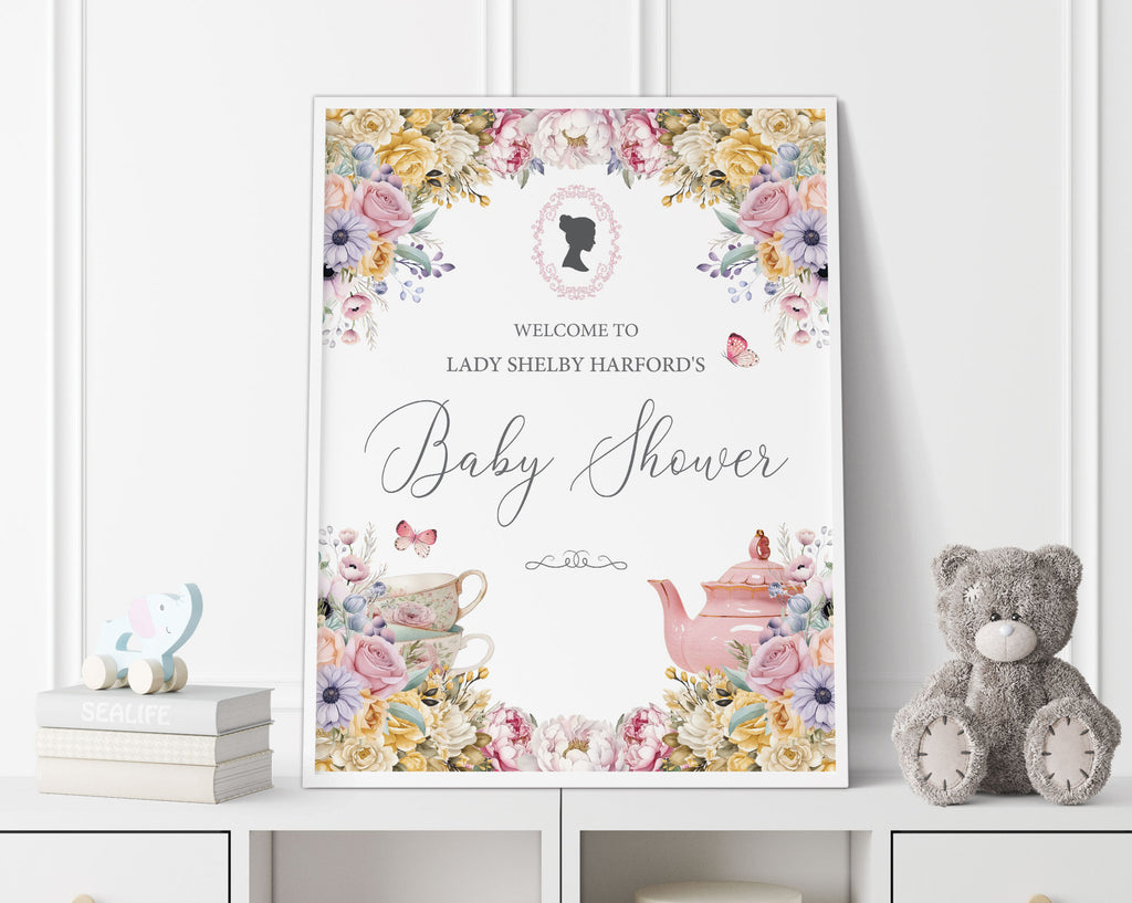 18 x 24 baby shower welcome sign with regency style cameo and pastel flowers, tea pot and tea cup graphics, in a white frame, leaning up against a white panelled wall next to a grey teddy bear and some books
