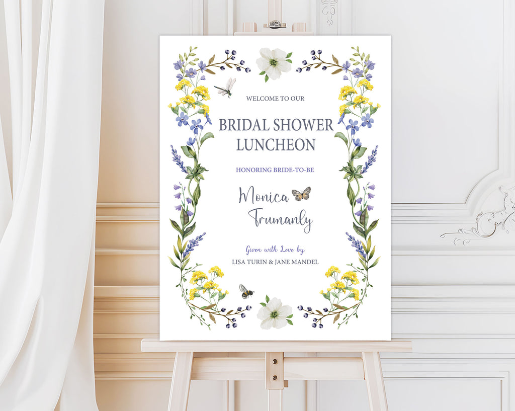 elegant wildflower and butterfly entrance sign for a bridal shower on a wooden easel in front of a white panelled wall and curtain