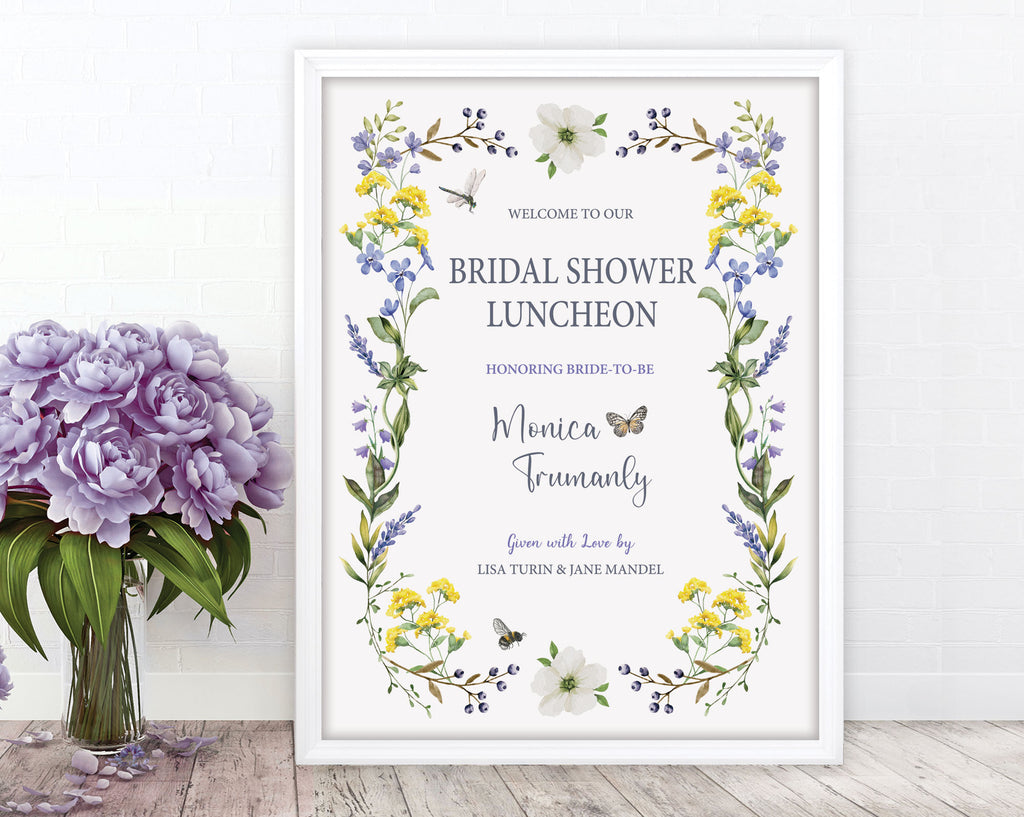 pretty blue purple and yellow flower bridal shower luncheon welcome sign with dragonfly, bee and butterfly graphics, in a white frame, leaning up against a white wall, next to a vase with purple flowers