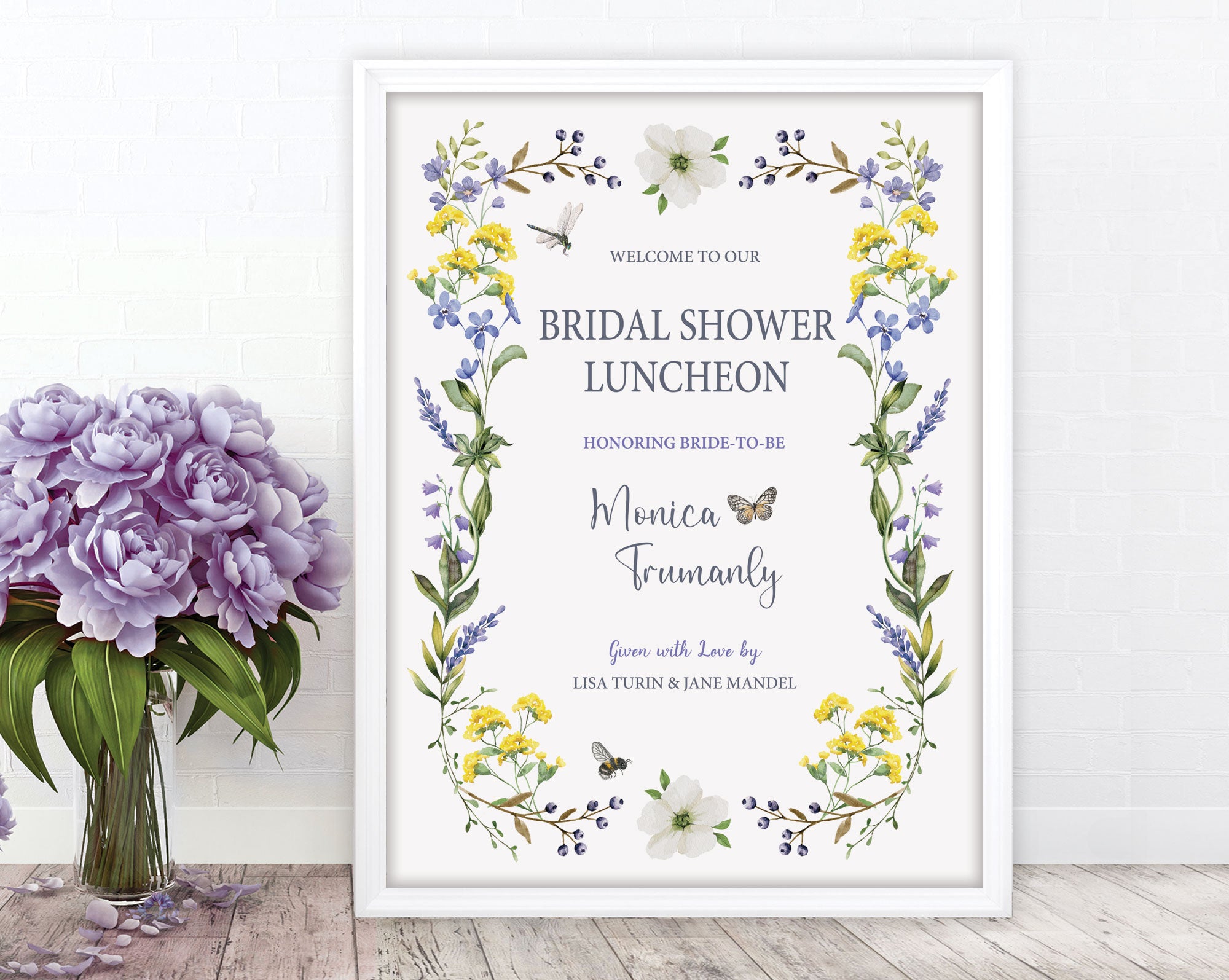 pretty blue purple and yellow flower bridal shower luncheon welcome sign with dragonfly, bee and butterfly graphics, in a white frame, leaning up against a white wall, next to a vase with purple flowers