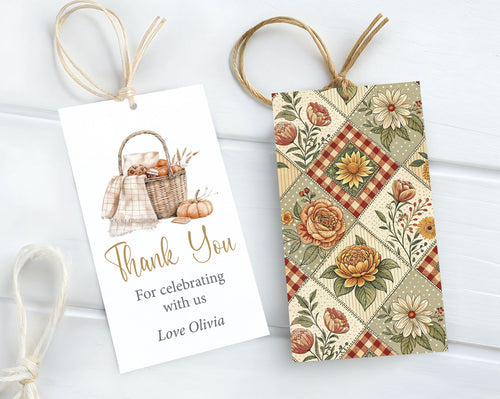 Two autumn-themed gift tags with twine loops, displayed on a white wood background. One tag is white with a watercolor illustration of a picnic basket, pumpkins, and the text 'Thank You For celebrating with us Love Olivia' and the other shows a quilt like patterned back.