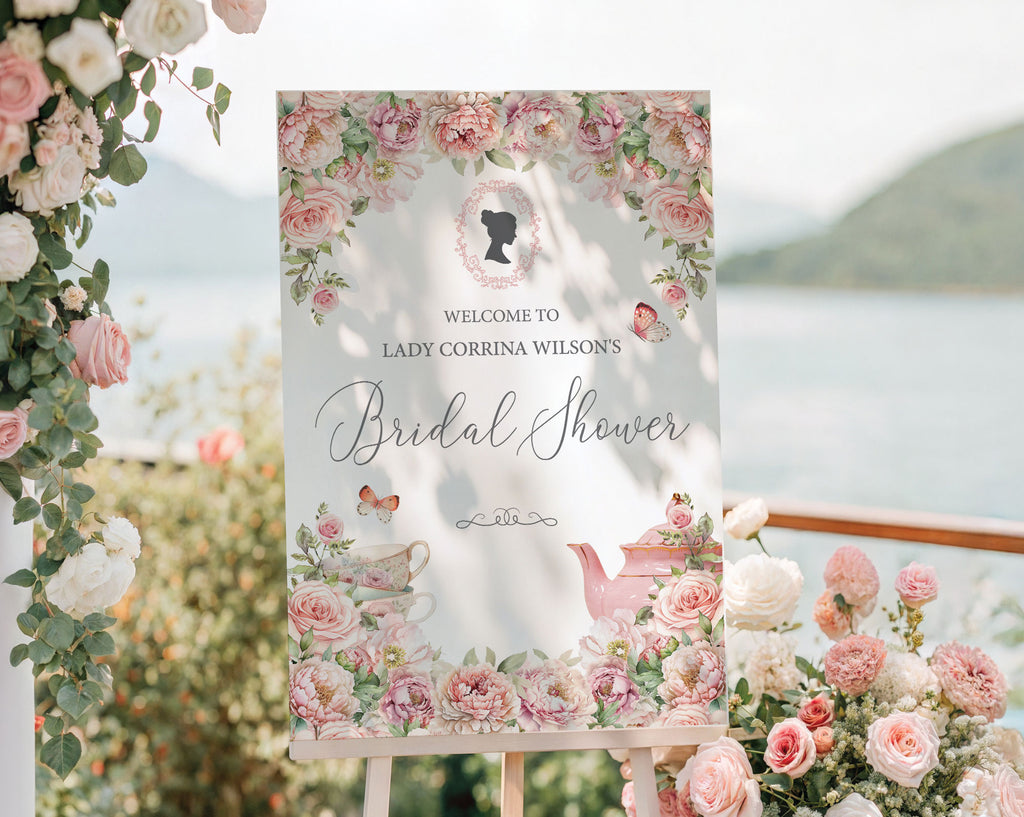 pretty pink flower welcome sign for a bridal shower, outside on a wooden easel in front of a lake backdrop next to trailing vines with pink and white flowers