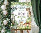 24 x 36 dinosaur and volcano party welcome sign on an easeal in front of a window with green curtains and some greenery with white balloons