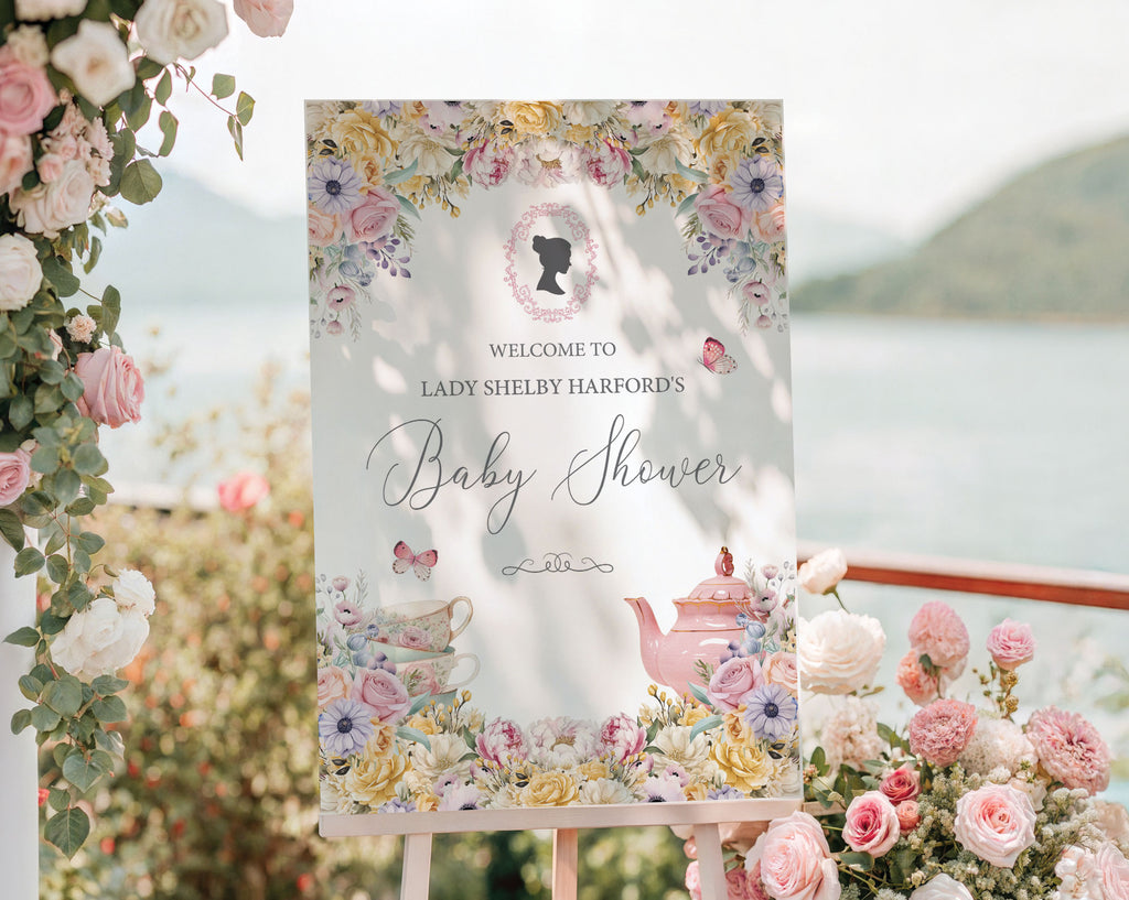 pretty pastel flower welcome sign for a baby shower, outside on a wooden easel in front of a lake backdrop next to trailing vines with pink and white flowers