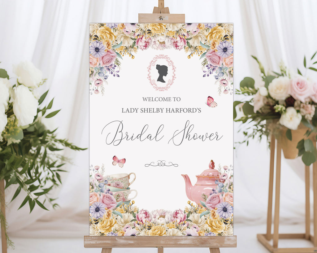pastel flower bridal shower welcome sign with regency style cameo on a wooden easel in front of a white curtain and some flowers on stands