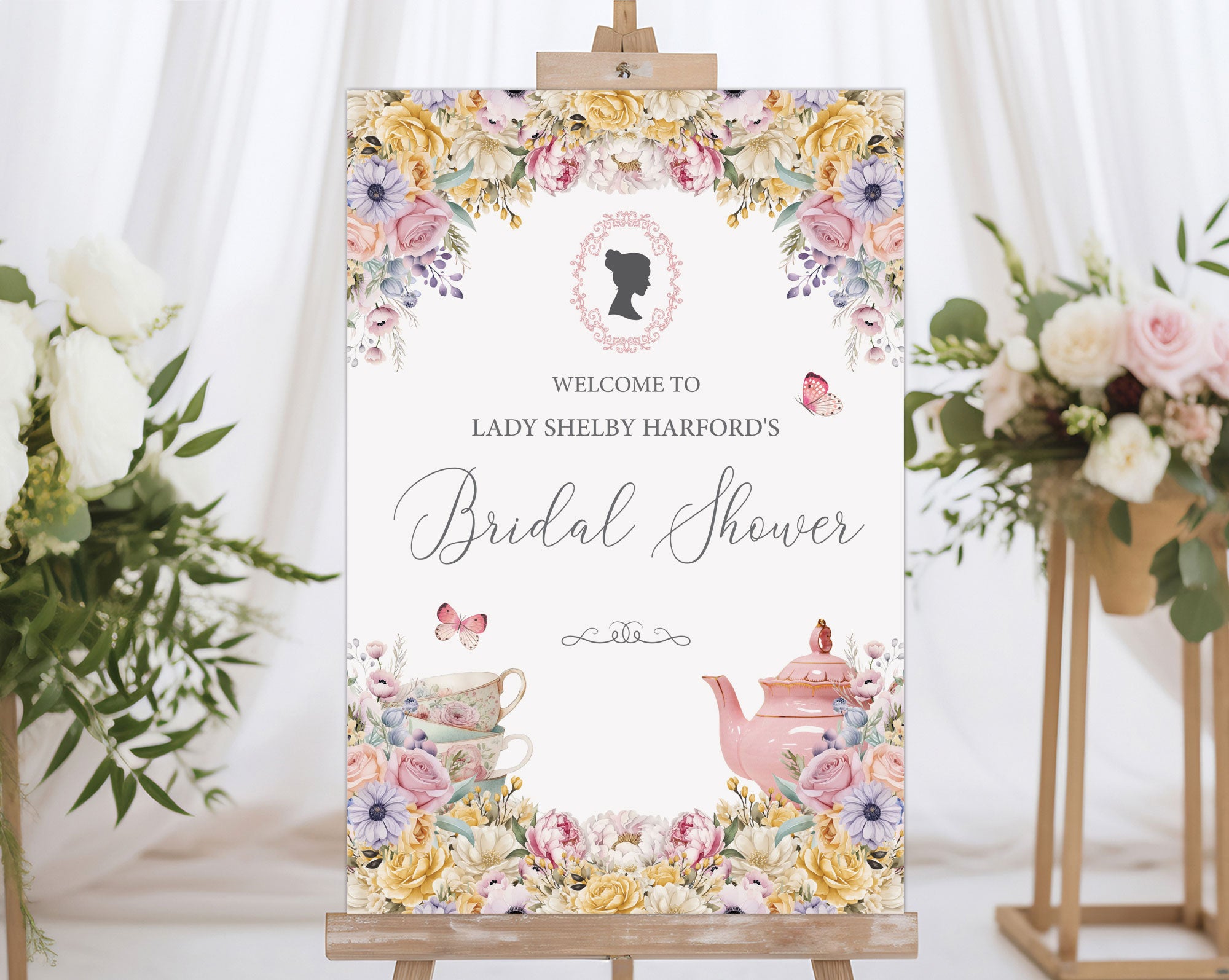 pastel flower bridal shower welcome sign with regency style cameo on a wooden easel in front of a white curtain and some flowers on stands
