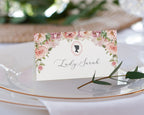 Place card with floral design and text 'Lady Carrington' on a white plate with greenery.