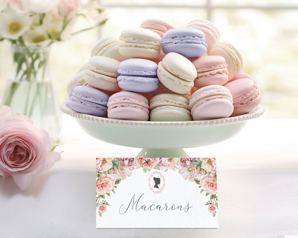 Pastel macarons on a white stand with a floral card below on a blurred floral background