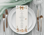A pretty vertical menu card with a rustic autumn theme, styled on a white plate with rose gold cutlery, a sage green napkin, and a glass on a gray wood table.