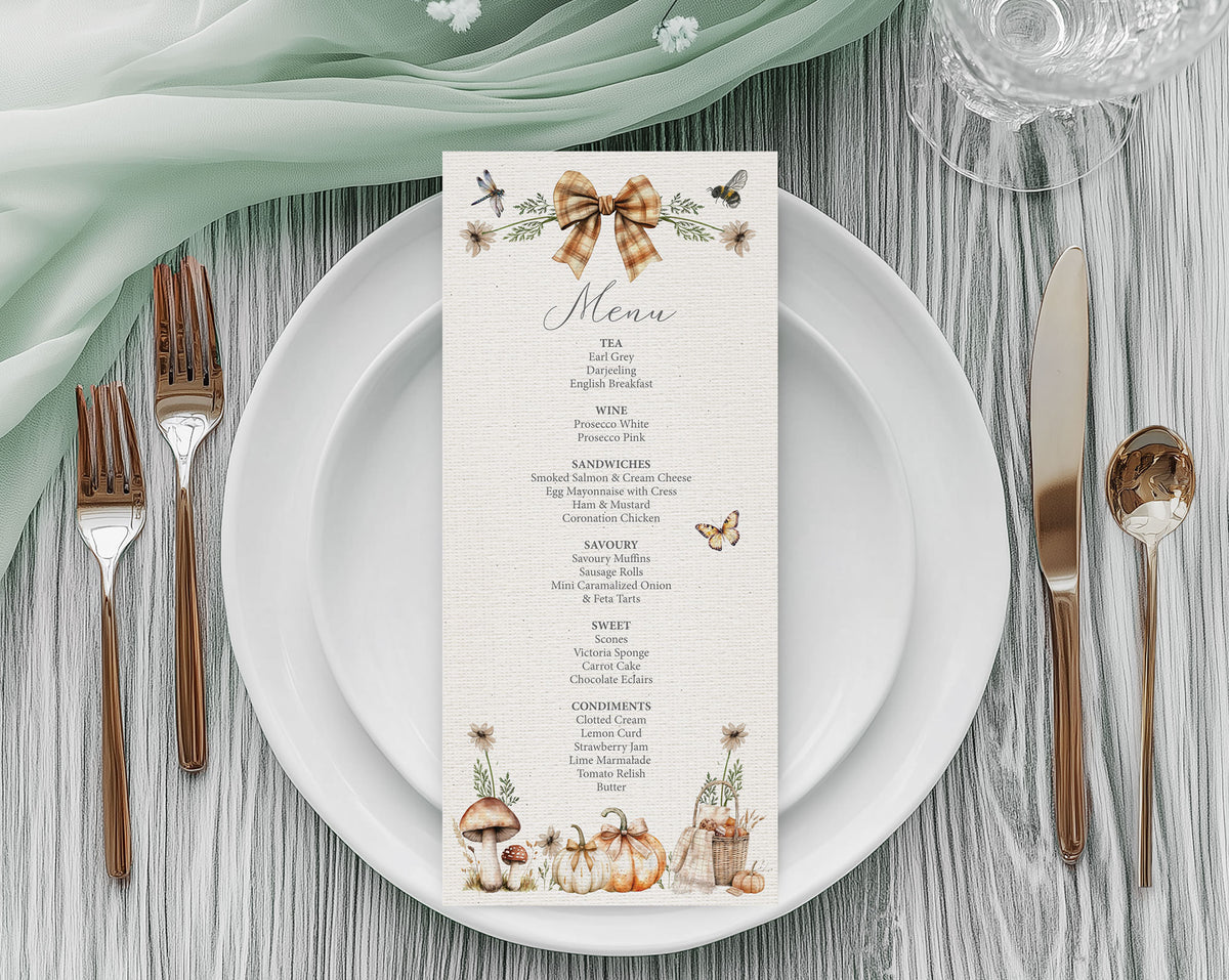 A pretty vertical menu card with a rustic autumn theme, styled on a white plate with rose gold cutlery, a sage green napkin, and a glass on a gray wood table.