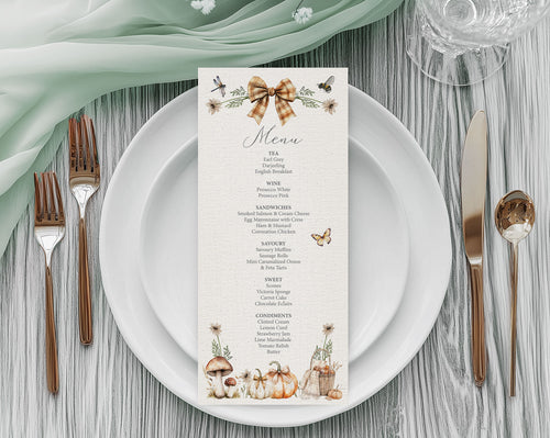 A pretty vertical menu card with a rustic autumn theme, styled on a white plate with rose gold cutlery, a sage green napkin, and a glass on a gray wood table.