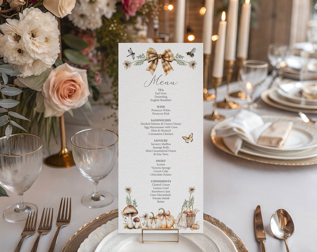 A vertical menu card with a rustic autumn theme, displayed on a table setting. The menu features a brown gingham bow illustration at the top and illustrations of pumpkins, mushrooms, and wildflowers at the bottom.
