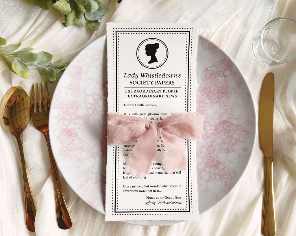 Pretty Dear Gentle Reader Ton Kids birthday Society announcement wrapped in a pink ribbon on a plate sitting on a silk white background with gold fork and knife