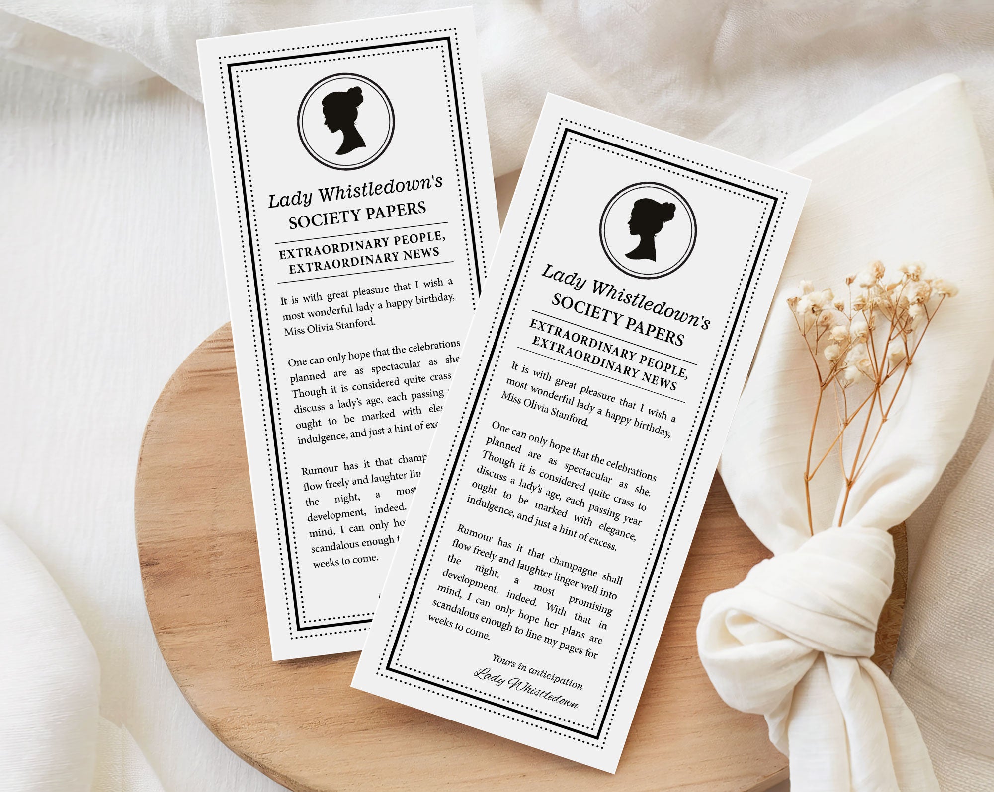two 'Lady Whistledown's Society Birthday Announcement Papers' on a wooden surface with a white fabric background.