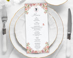 Menu card with pink floral design on a white plate with gold rim and silverware.