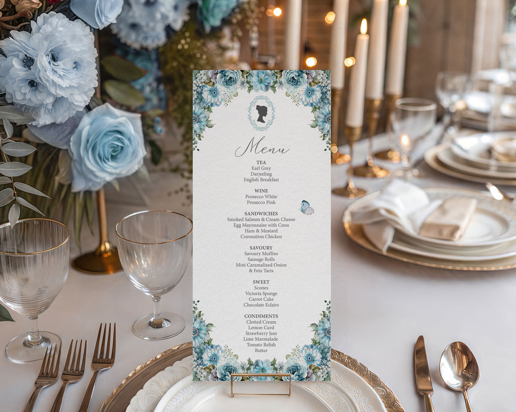 Pretty tea table set up with a dusty blue flower, bridgerton-inspired 4 x 9 menu in a gold stand sitting on a plate