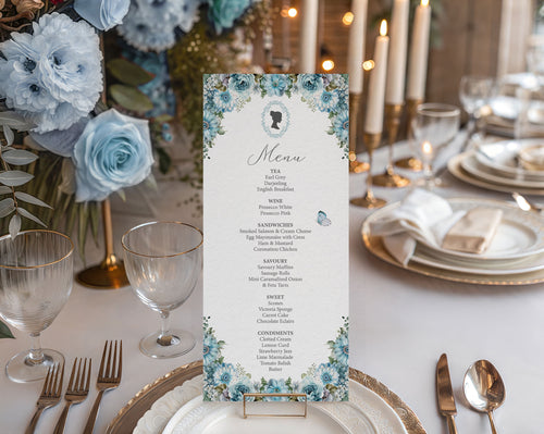 Pretty tea table set up with a dusty blue flower, bridgerton-inspired 4 x 9 menu in a gold stand sitting on a plate