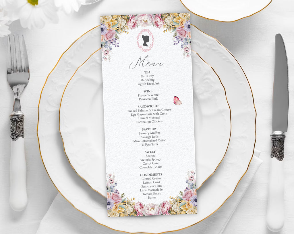 Menu card with floral and cameo design on a white plate with gold rim, silverware, and white flowers.