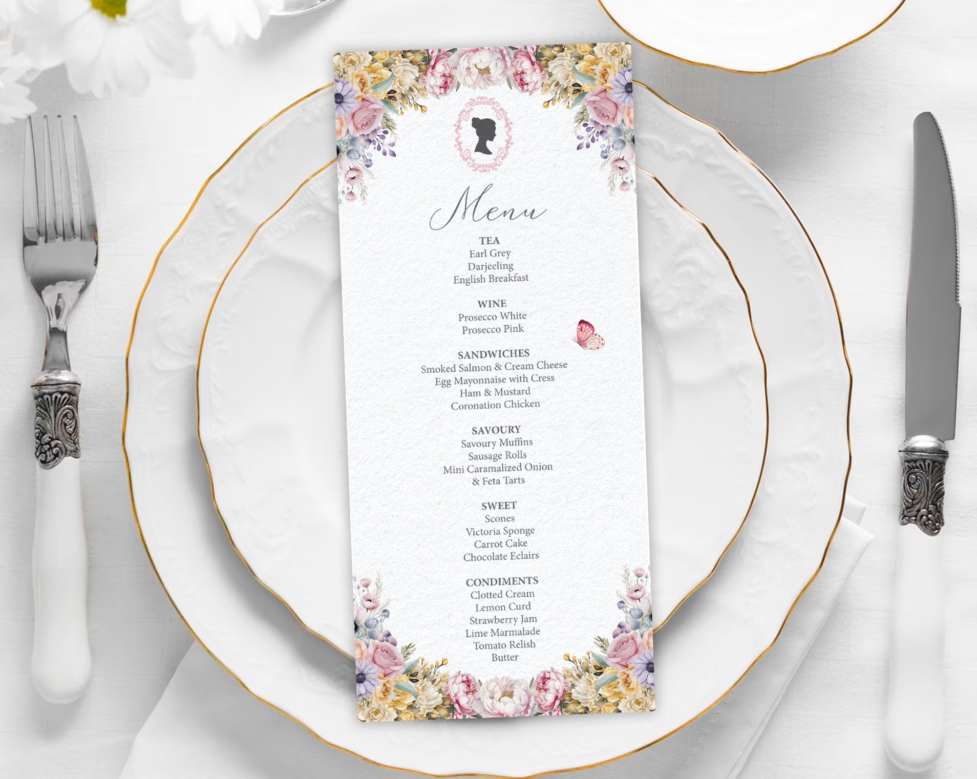 Menu card with floral and cameo design on a white plate with gold rim, silverware, and white flowers.
