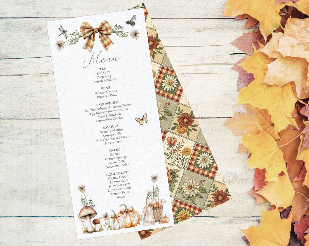 A fall-themed printed menu card with floral and mushroom illustrations, placed on top of a matching patterned paper sheet over a whitewashed wood surface with scattered autumn leaves around it.