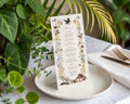 an enchanted menu with a recycled finish standing up on a plate in front of some greenery on a white table
