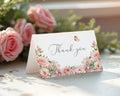 Floral 'Thank you' card with blush pink flowers and a butterfly design on a white surface with pink roses in the background.