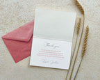 White card with 'Thank you' message on a textured surface with a pink envelope and wheat stalks.