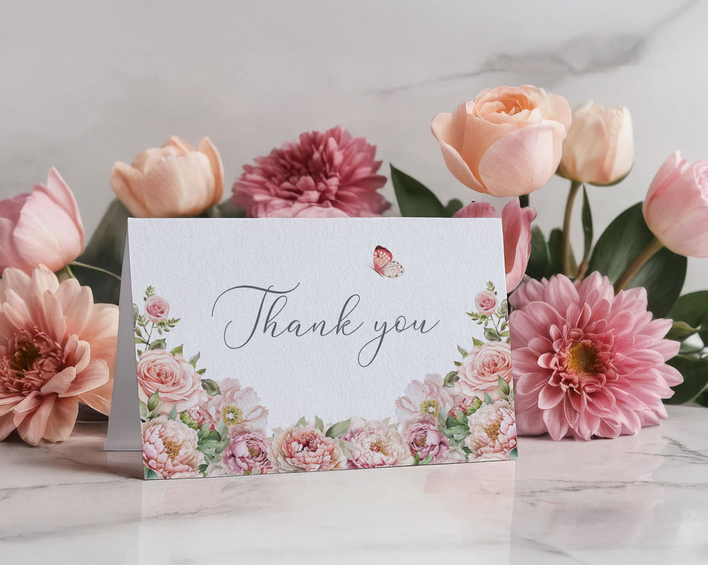 Thank You tent card with 'Thank you' text and butterfly design surrounded by pink flowers on a marble surface