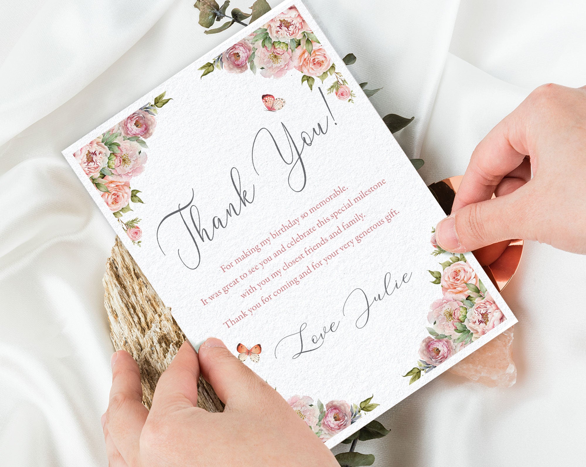Card with floral design and text held by hands on a light background
